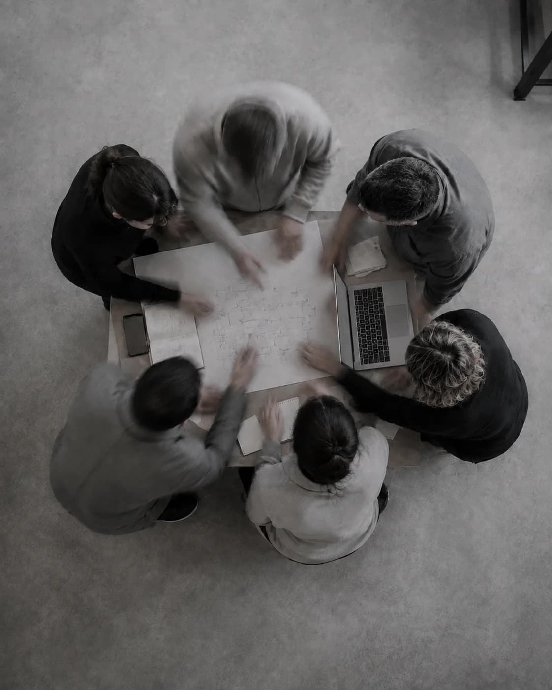 Illustrative overhead view of a group collaborating around a worktable, with hands in motion.